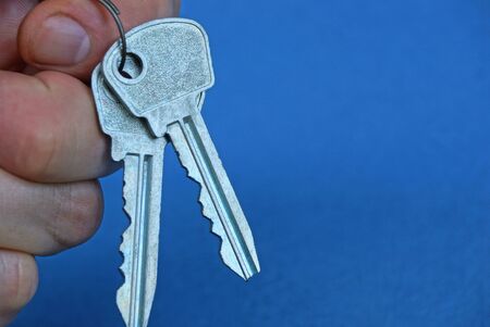 two gray door keys are hanging on the fingersの写真素材
