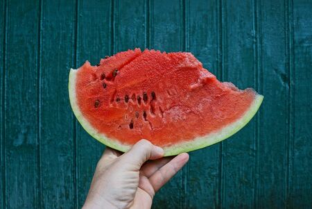 hand holds a piece of watermelon against a green wall