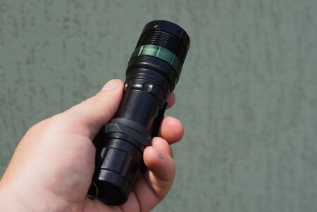 hand holds a black metal flashlight on a gray background