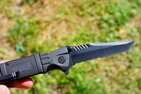 one black folding knife in hand on a background of green grass on the street