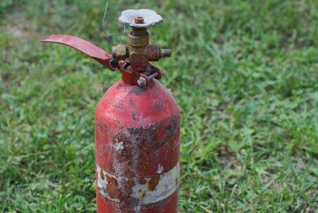 red old fire extinguisher with a valve on a background of green grassの写真素材