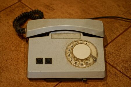 old gray plastic phone with a cord stands on a brown tableの写真素材
