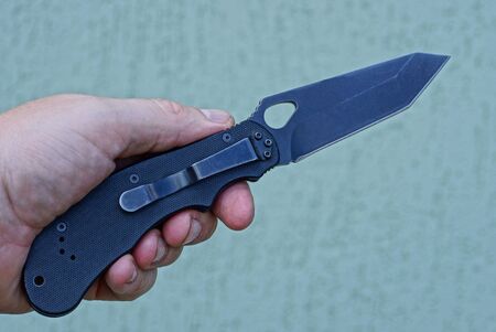 hand holds a one black folding knife on a gray background