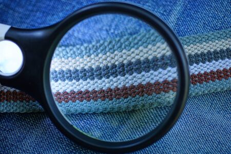 black magnifier enlarges striped colored belt on blue cotton fabricの写真素材