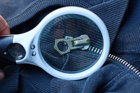 a white magnifier magnifies a gray metal zip on black clothesの写真素材
