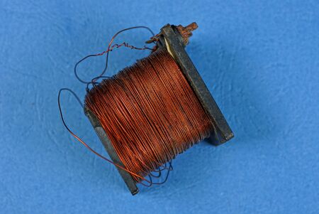 black old coil with red copper wire lies on a blue table