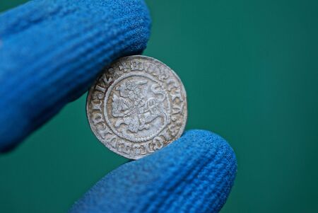 old white medieval silver coin in fingers in blue gloves on a green background
