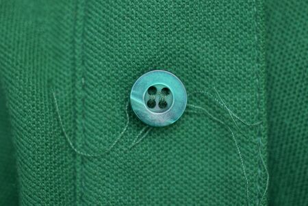 one plastic button with threads on a green clothの写真素材