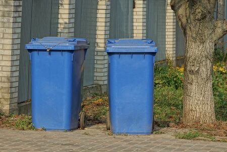 two blue plastic garbage cans on the street near a gray fenceの写真素材