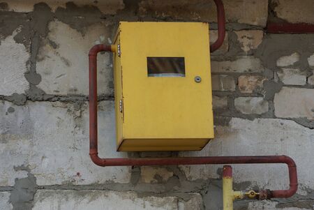 yellow metal box with gas meter and brown pipe on a gray wallの写真素材