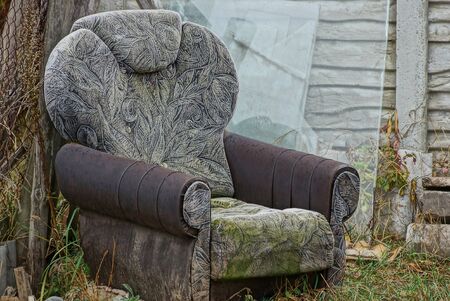 one old dirty chair stands outside in the grass against the wall