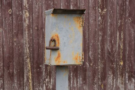 gray iron electric box in rust with padlock against a brown wooden wall
