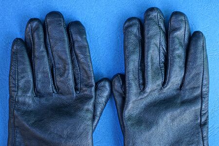 two black leather gloves lie on a blue table