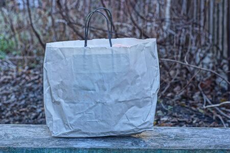 one white paper bag stands on a gray wooden table in the streetの写真素材