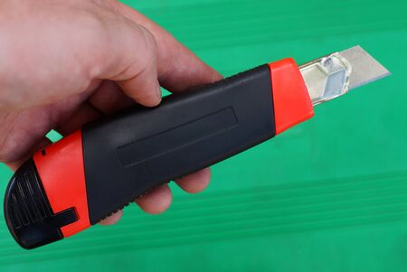 hand holds a one stationery knife with a blade on a green background