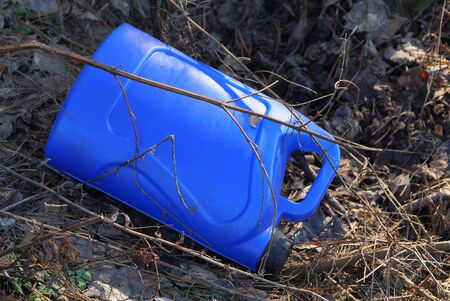 trash from a one blue plastic canister lies in the dry grassの写真素材