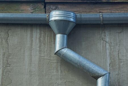gray metal pipes of a drain on a concrete wall of a building