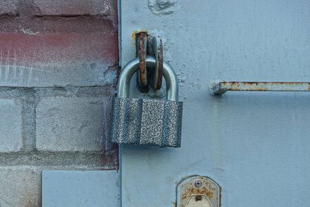 one large gray padlock on an iron gate and a brick wall