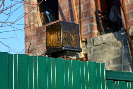 one yellow square signal light on a green metal fence in the street