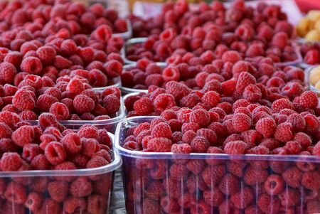 plastic boxes full of red ripe raspberries on a table in a marketの写真素材