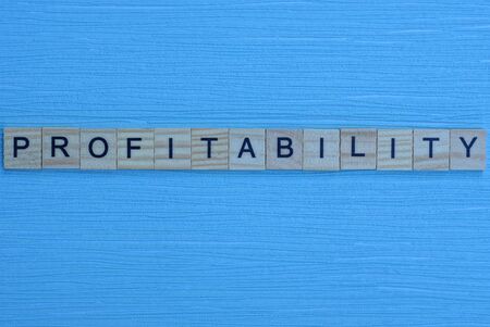 gray word profitability from small wooden letters on a blue tableの写真素材