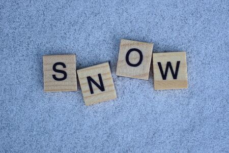 word made of small gray wooden letters lies on white snowの写真素材