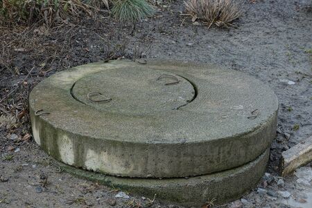 a large gray and wet concrete sewer hatch stands on the ground outside