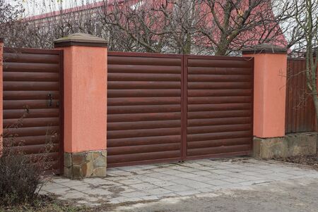 brown closed gate and part of a fence of wooden boards and concrete on a rural street