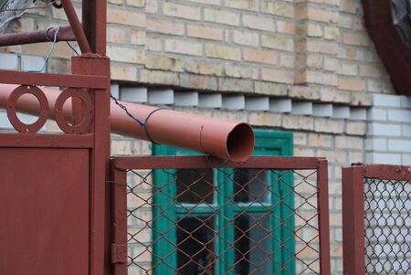 brown plastic drainpipe on an iron mesh fence on a rural streetの写真素材