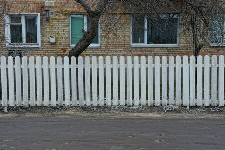 white long fence made of wooden planks on the street in front of a brick brown house on the streetの写真素材