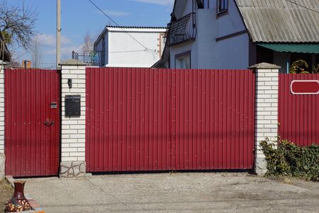 large red metal gate and white brick fence on a rural street on a sunny dayの写真素材