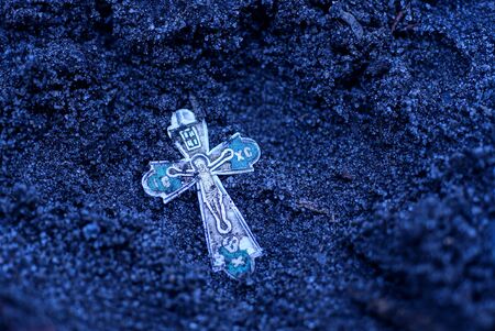 one old silver christian cross lies in the black earth on the streetの写真素材