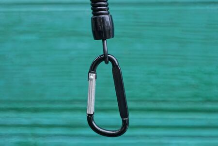one black metal carabiner clasp on a plastic wire on a green backgroundの写真素材