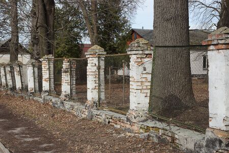 old ruined fence on a rural street of white bricks and metal meshの写真素材
