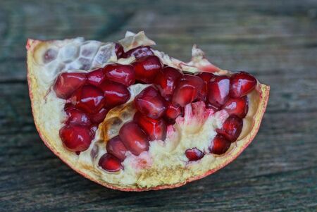 a piece of pomegranate fruit with red small berries lies on a gray tableの写真素材