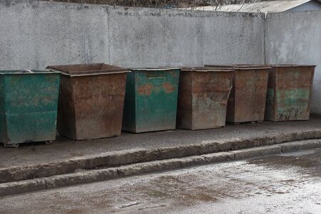 a row of old iron rusty garbage cans stand against a gray concrete wall on asphalt on the streetの写真素材