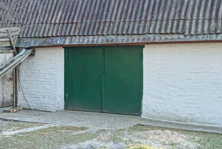 facade of a white brick garage with green iron gates under a gray slate roof on the streetの写真素材