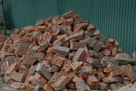 a pile of pieces of old red bricks in gray concrete on the street against a green wall