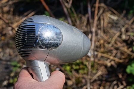 hand holds old gray plastic hair dryer outdoors in nature on a sunny dayの写真素材