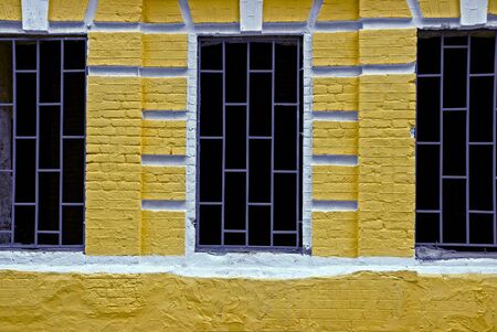 three old black windows with gray iron bars on the yellow brick wall of the houseの写真素材
