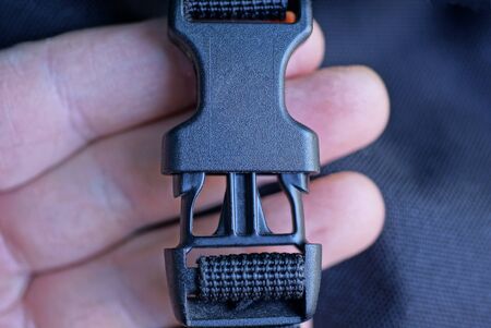 fingers hold a closed black plastic carabiner on a harness made of fabricの写真素材