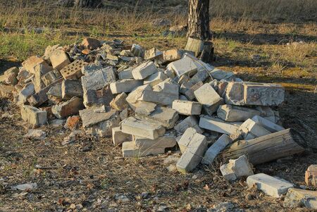 a large pile of rubbish from pieces of gray concrete and bricks lies on dry grass and land on nature