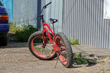 one red sports bike with black tire is standing outside against a gray fence wall on a sunny dayの写真素材