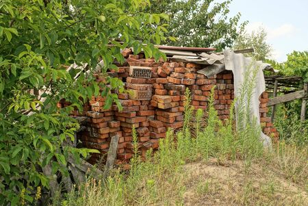 a pile of old red bricks overgrown with green grass and vegetation on the streetの写真素材