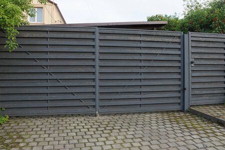 architecture of closed gray wooden gate on the sidewalk on a rural street