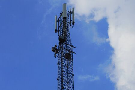high black iron pole with telephone antennas and transformers against the sky and clouds