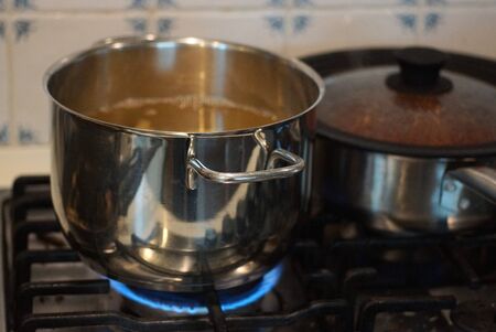 an open gray metal pan stands on the stove and is heated by a blue gas fire in the kitchen