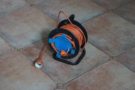 a black coil with an orange extension cord is on a brown tile in the roomの写真素材