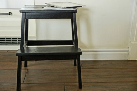 one black wooden stool stands against a gray wall on a brown floor in the room