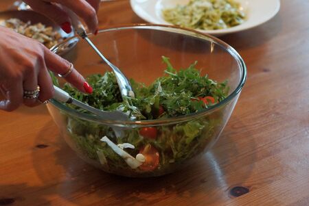 woman hands with fork and spoon pick up salad from a glass plate on a brown wooden tableの写真素材